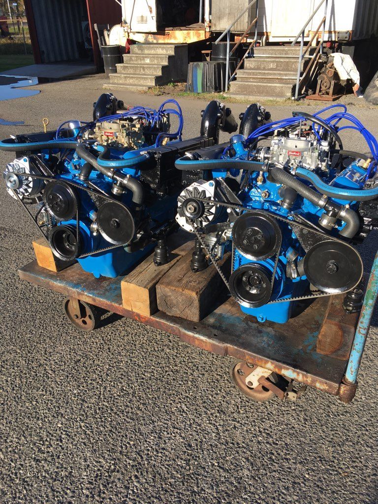 Two blue boat engines on a metal cart. Black pulleys and chrome accents. Outdoors.