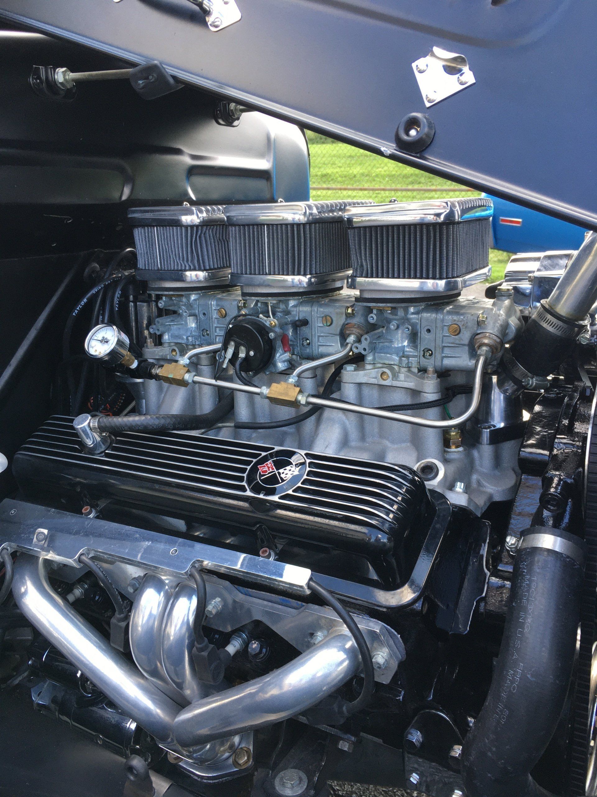 Close-up of a car engine with three carburetors, chrome headers, and black valve covers.