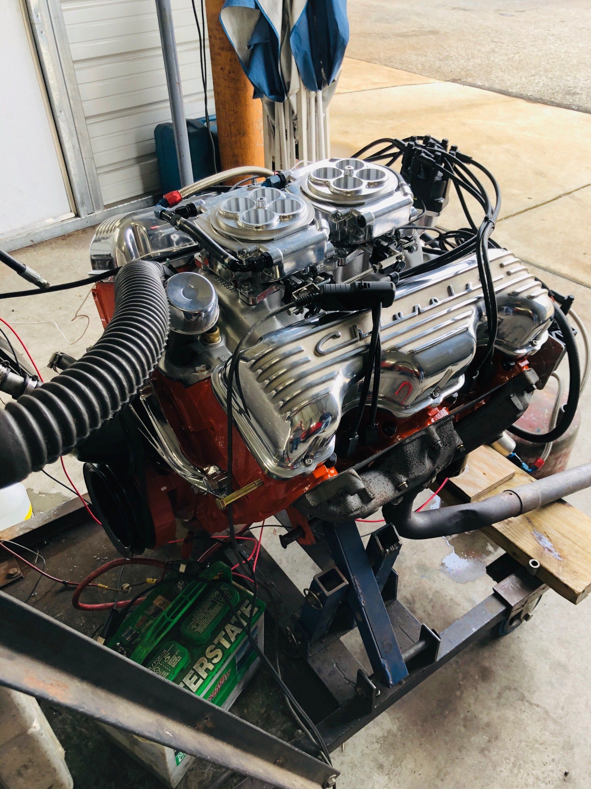 Chrome engine, dual carburetors, red block, on a metal stand with green battery.