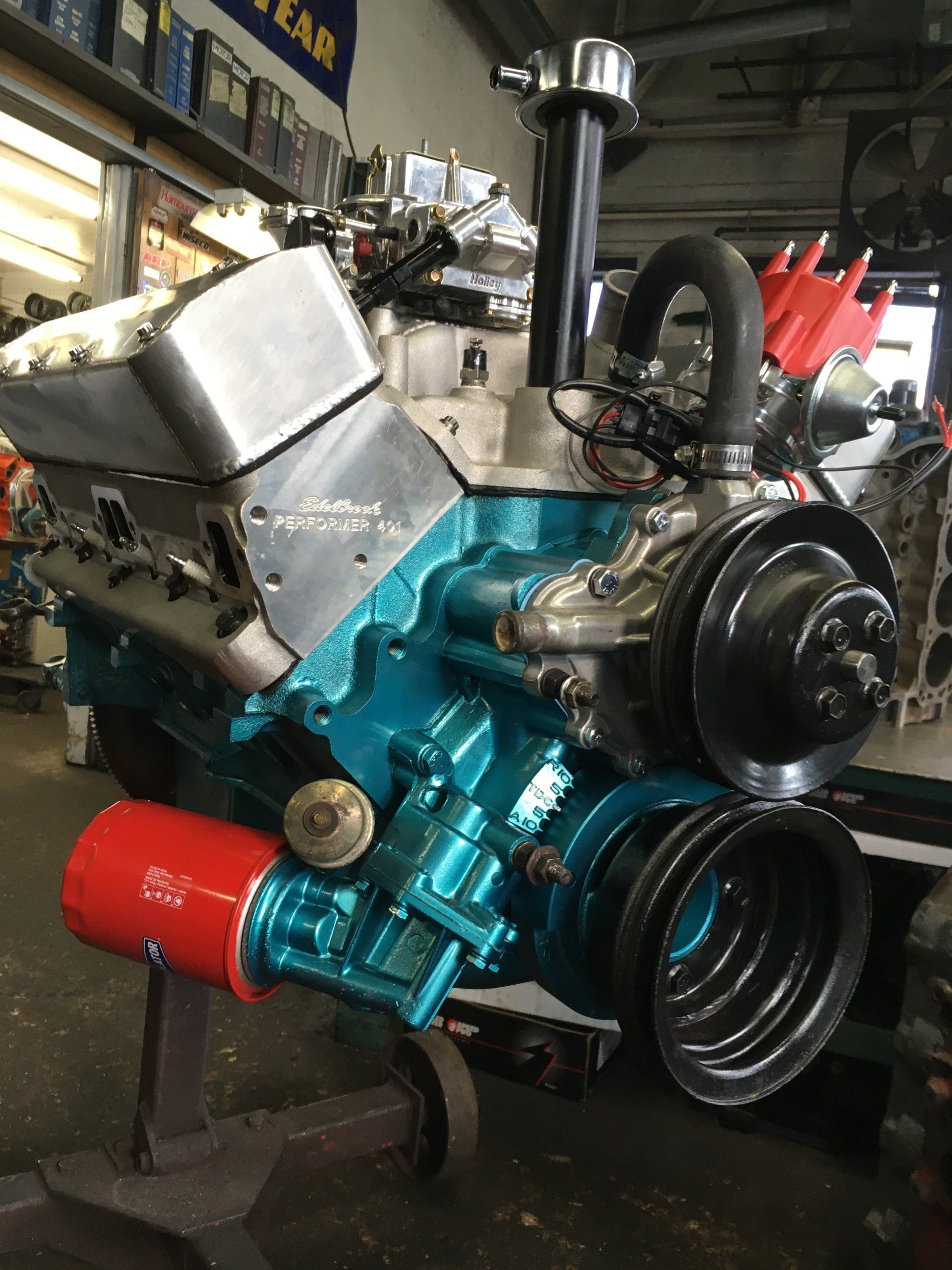 Blue engine with red filter, silver valve covers, black pulleys, inside a shop.
