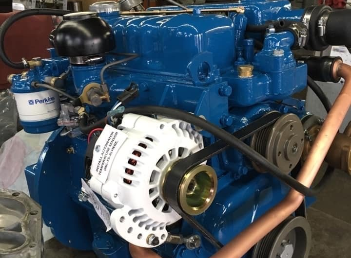 Blue marine engine with a white alternator, copper pipes, and a black belt.