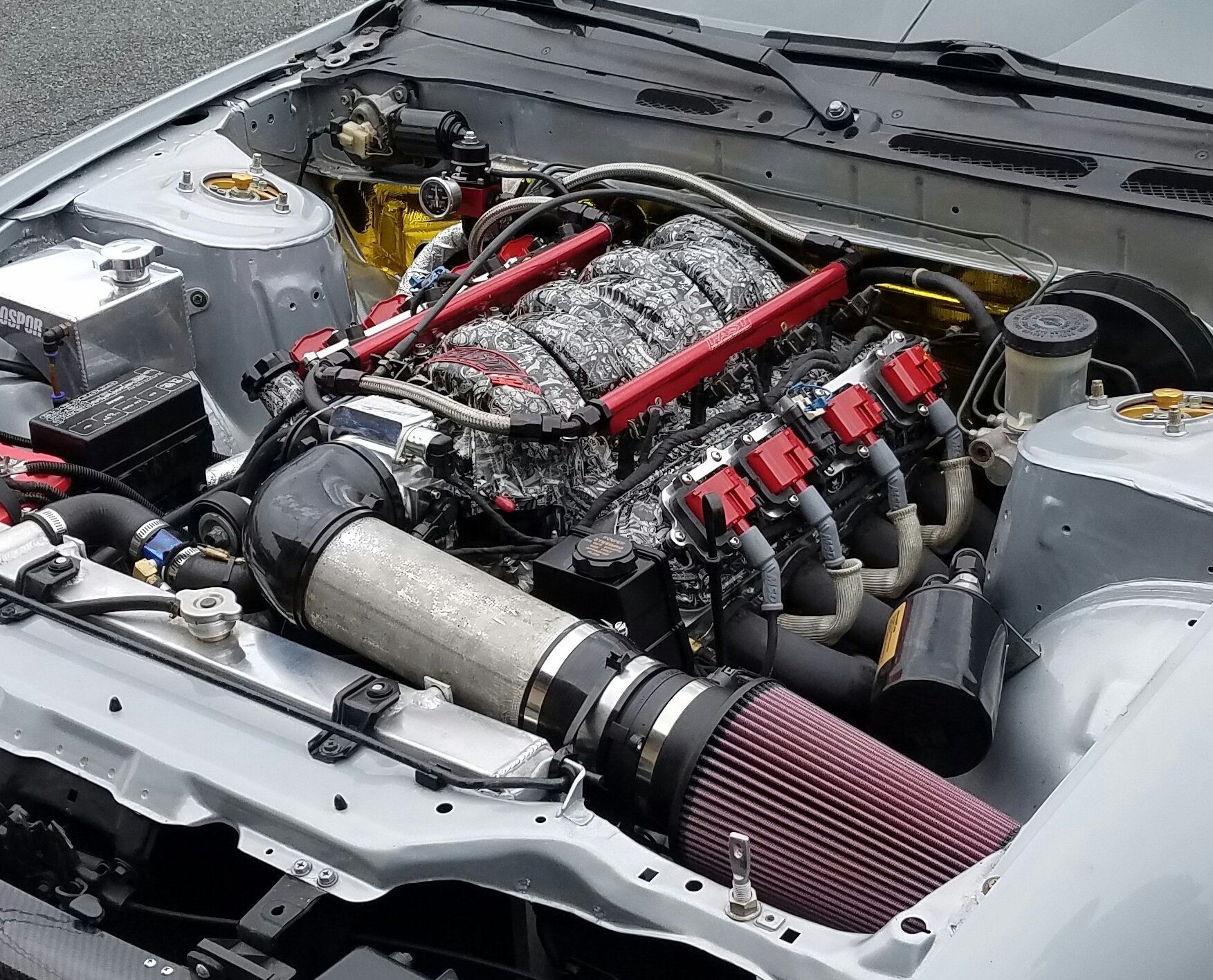 Silver car engine with red air filter and tubes, silver and black components visible.