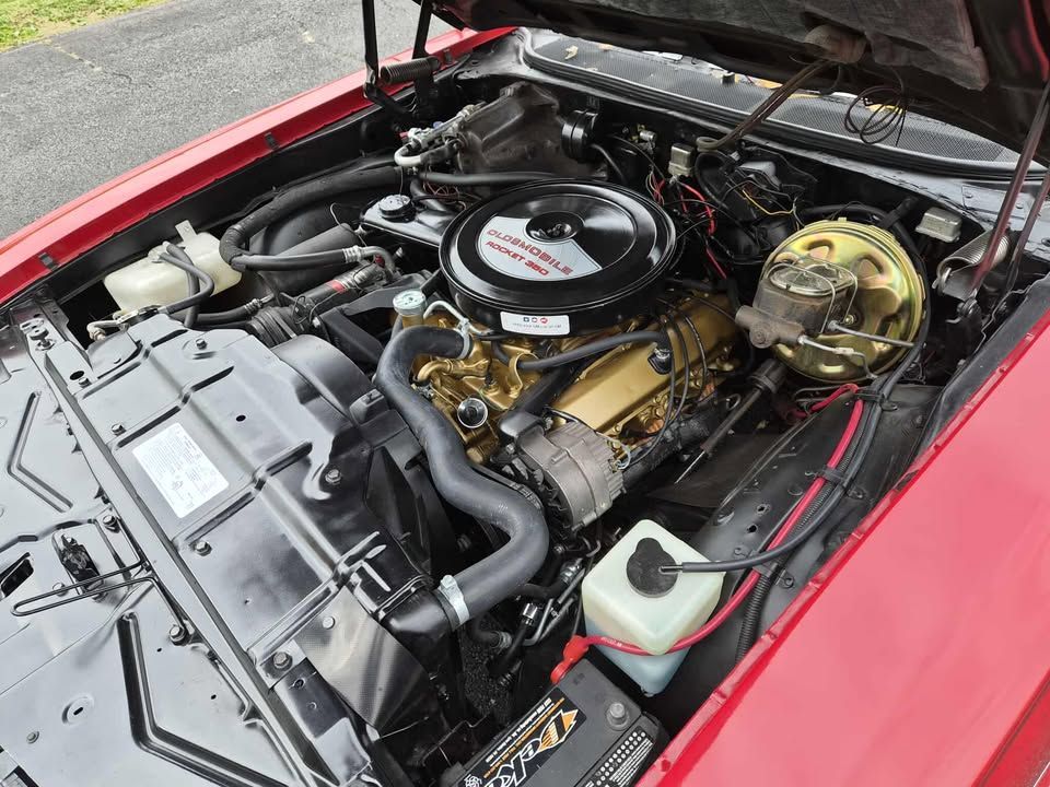 Red classic car engine bay, gold engine, black air cleaner, and various engine components.