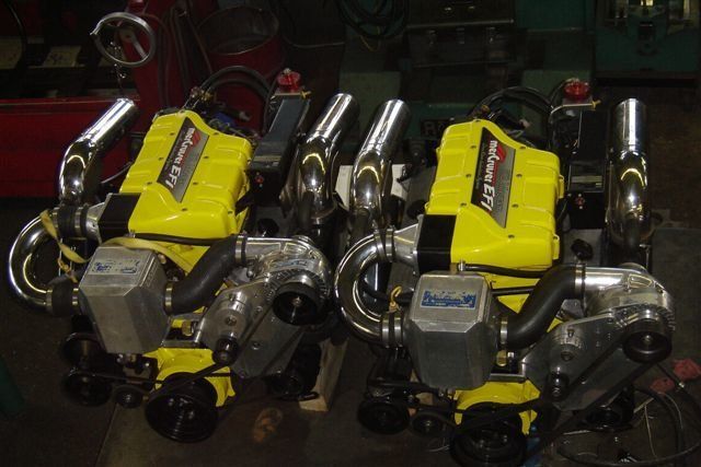 Two yellow and black marine engines with chrome exhaust manifolds and silver intakes.