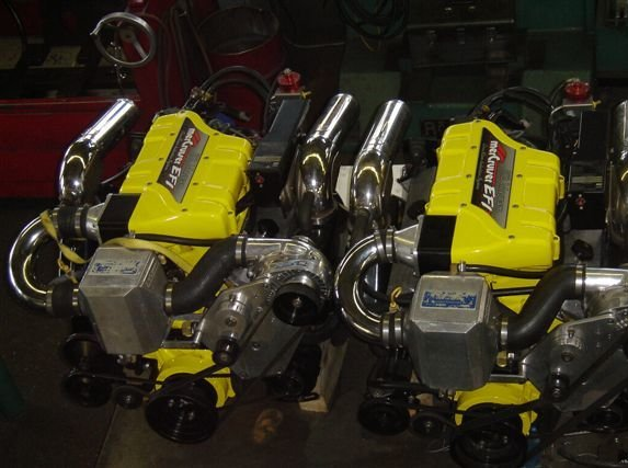Two yellow and gray boat engines with chrome exhaust pipes, possibly in a workshop.