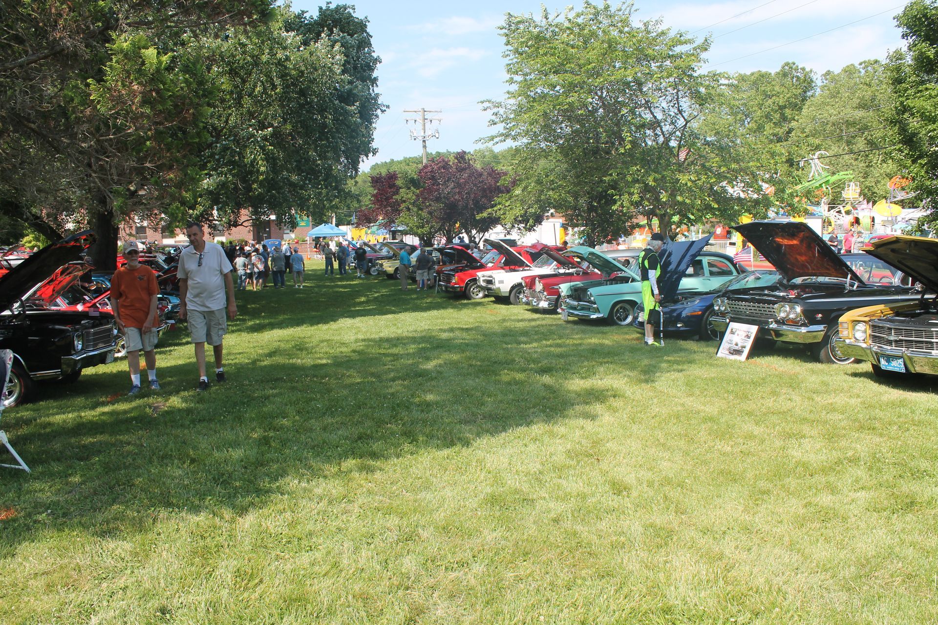 Classic cars on display at an outdoor event; people walking on grass; sunny day.