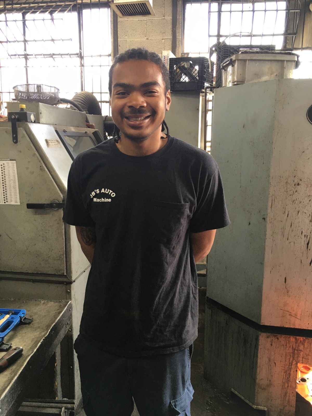 Smiling person in black shirt standing in a workshop with large industrial machines.