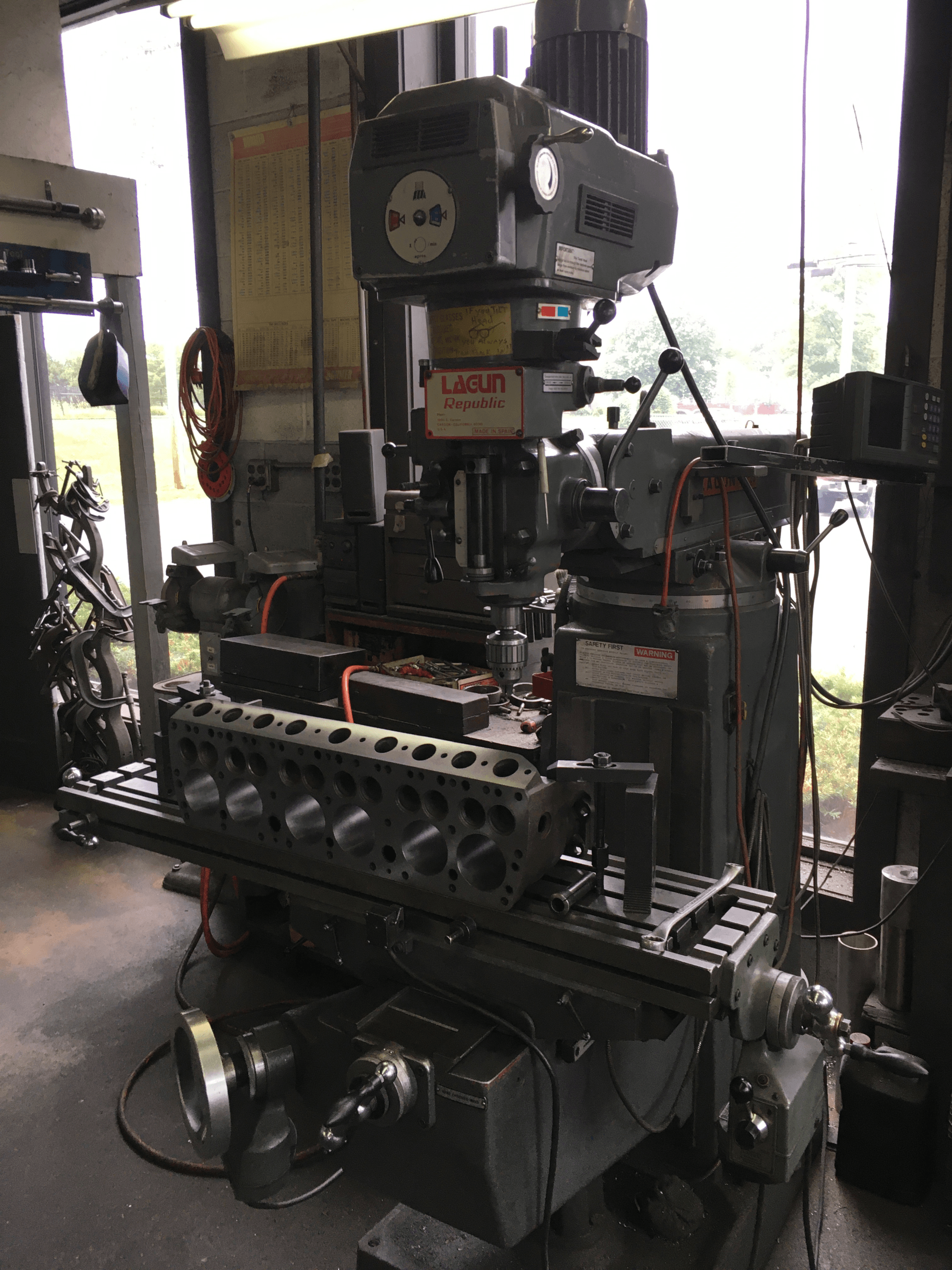 A milling machine in a workshop holding a large engine head. Gray machine, natural light.