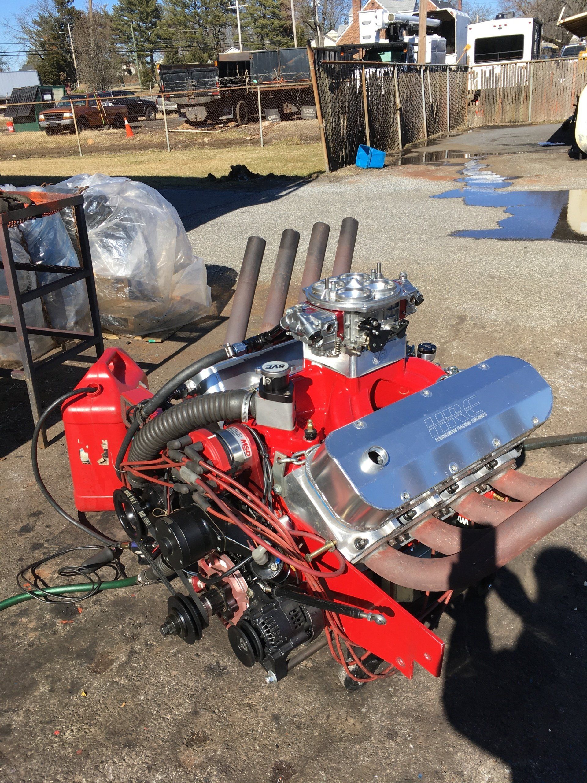 Red engine with chrome accents, including headers, on a stand outdoors.