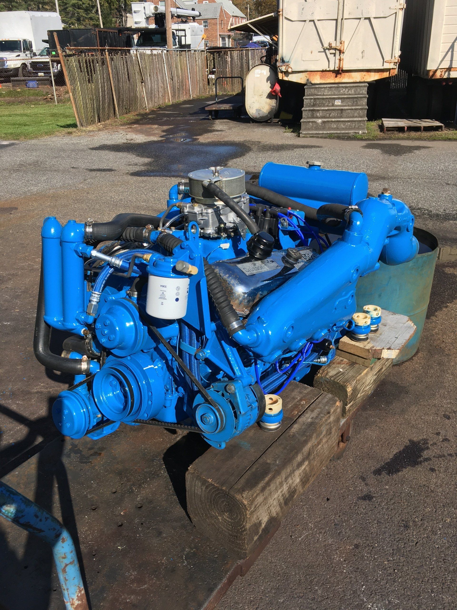 Blue boat engine, sitting outdoors, on a wooden base.