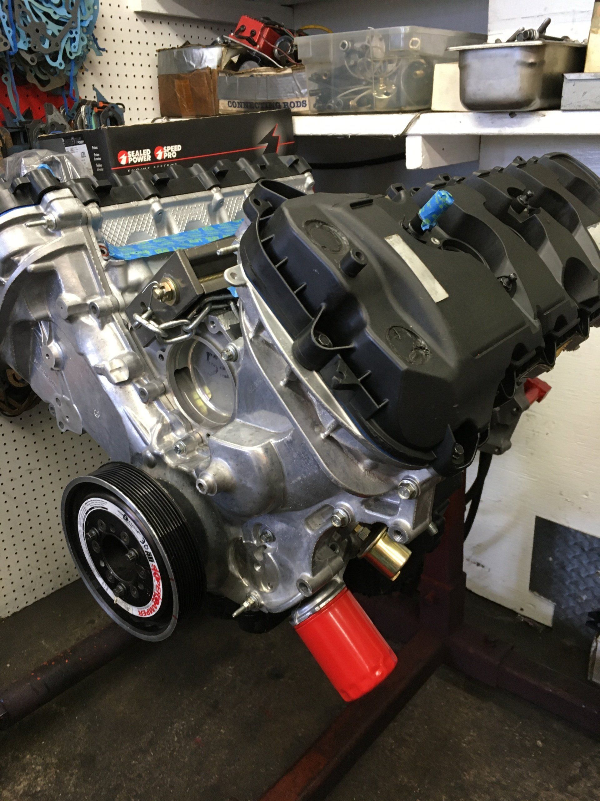 Engine with black cover, red filter, silver parts, on a stand in a shop.