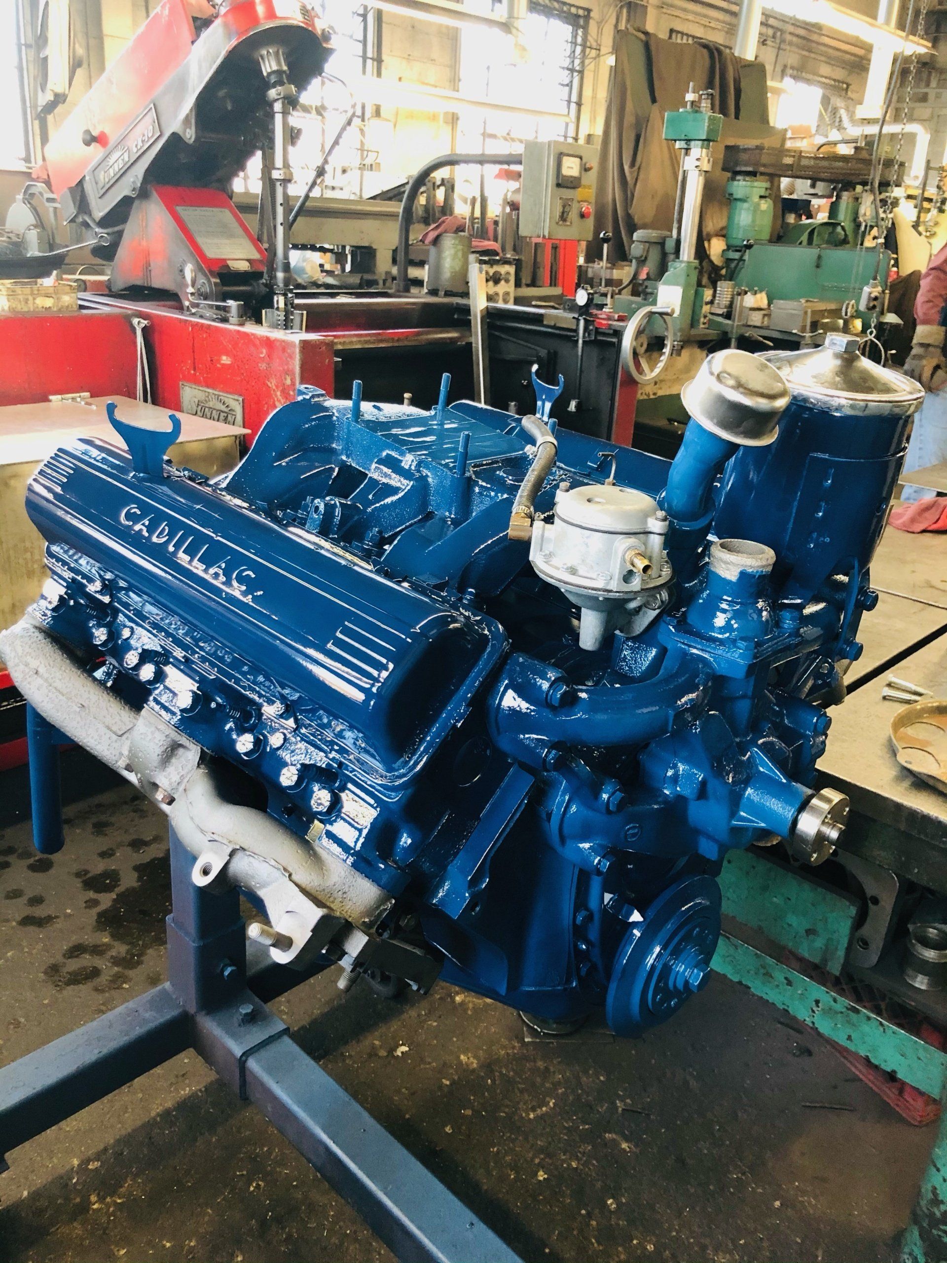 Blue Cadillac engine on a stand in a garage.
