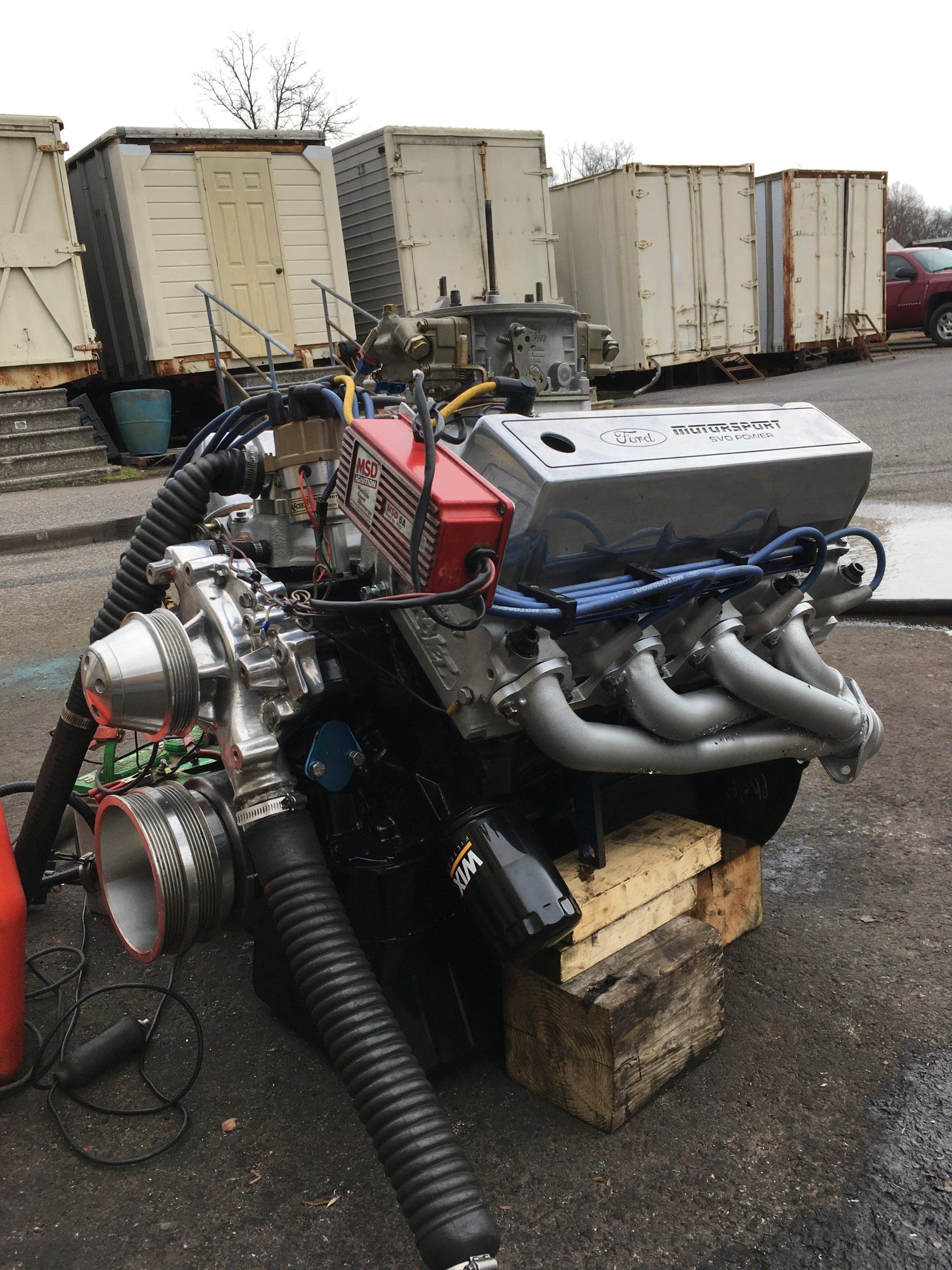 Engine with turbocharger on wooden blocks, outdoor setting. Black, silver, and red components.