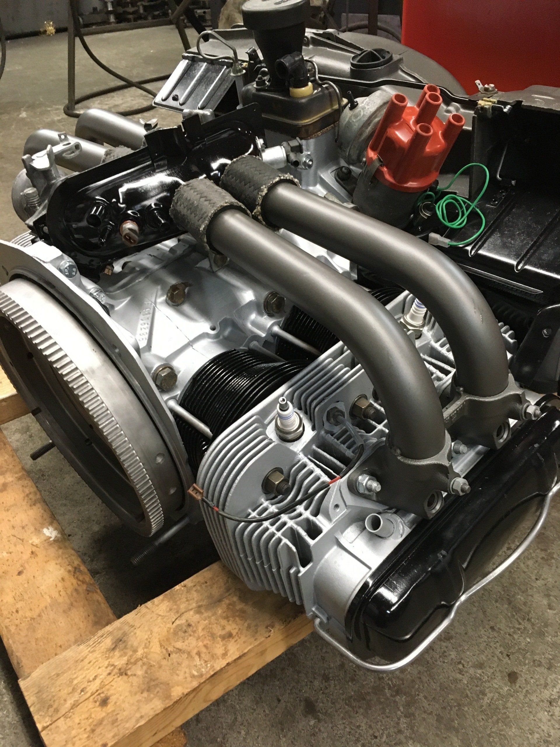 Air-cooled engine on a wooden pallet. Silver cylinders, black exhaust pipes, red distributor cap.