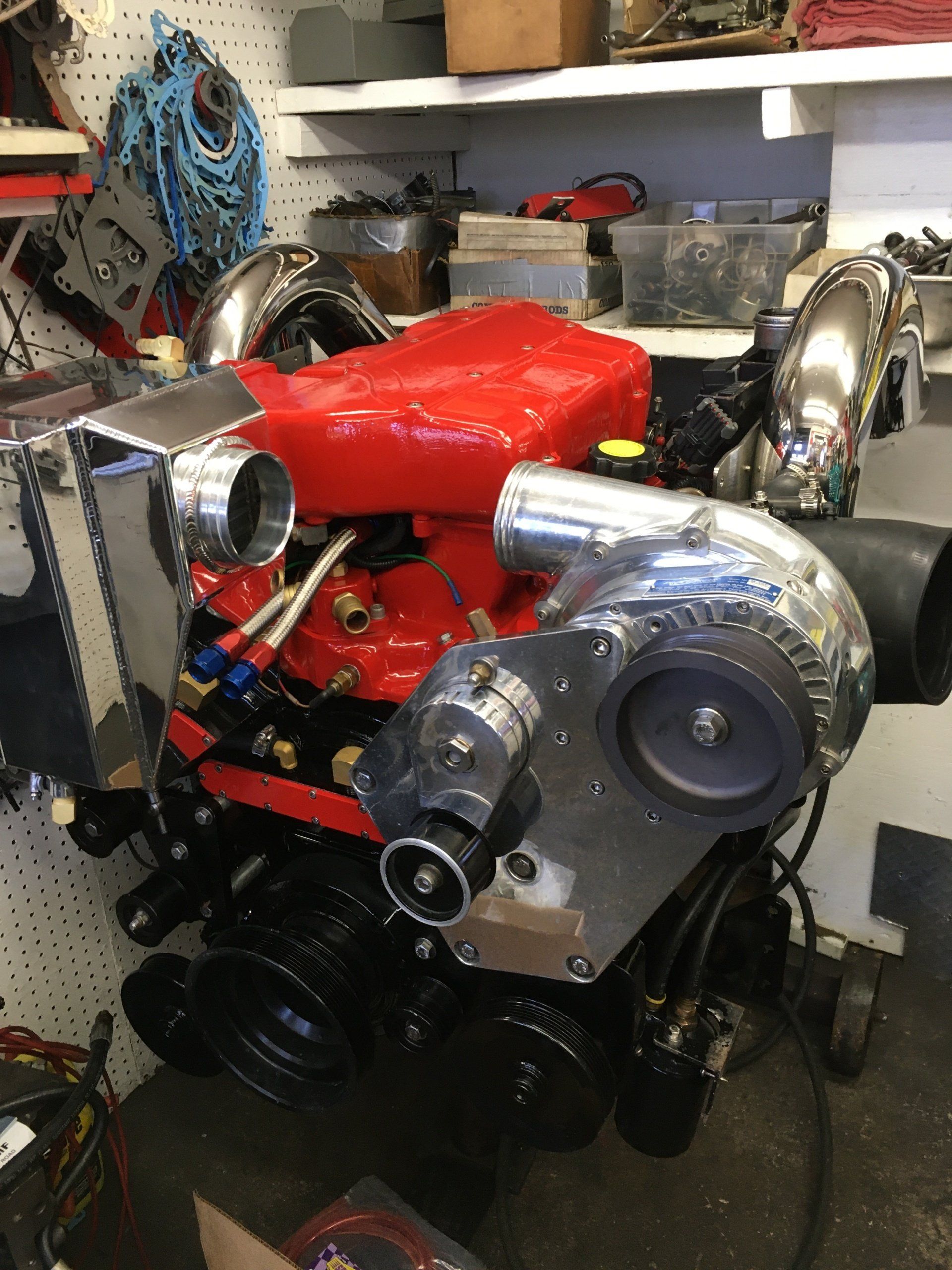 Red engine with silver turbochargers and piping; shop setting with tools and shelves.