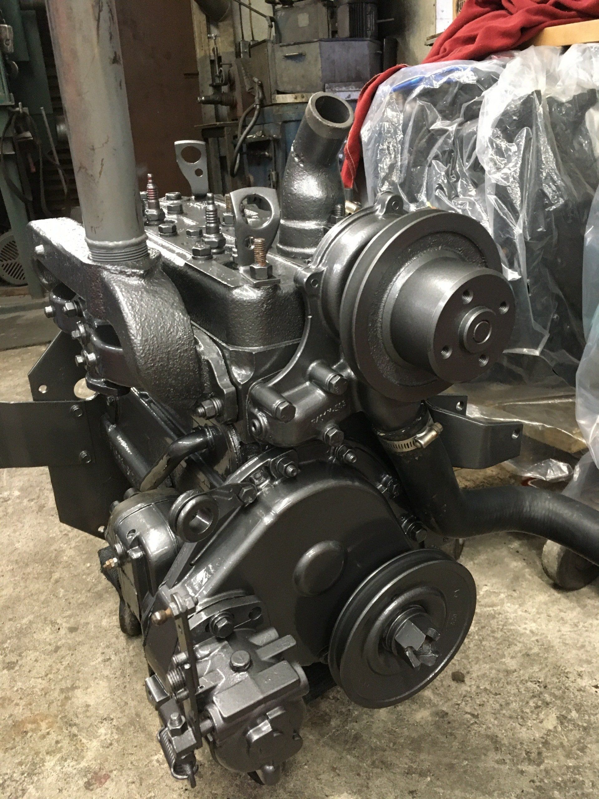 Black engine, likely diesel, with various components, pulleys, and exhaust manifold in a workshop setting.