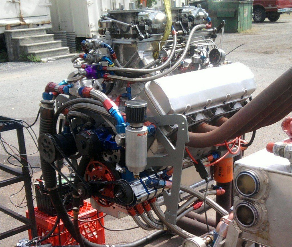 Large racing engine with numerous tubes and wires. Lifted over a frame, outdoors.