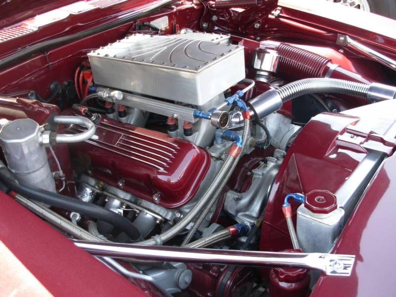 Close-up of a maroon car engine with custom parts, including a large air intake and shiny pipes.