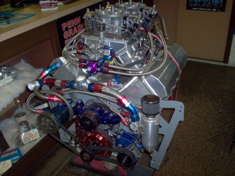 High-performance engine with multiple carburetors, intricate tubing, and pulleys; displayed indoors.
