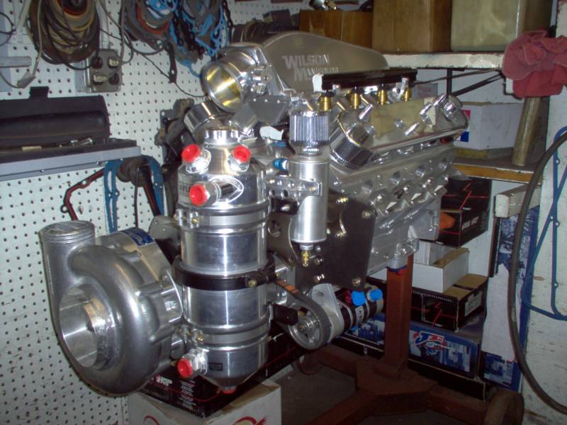 High-performance, chrome car engine with a large turbocharger, assembled on a stand in a garage.
