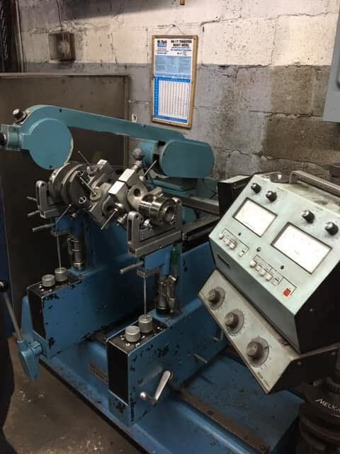 Blue industrial machine with dials and a mechanical arm in a workshop setting.