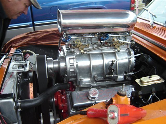 Orange hot rod engine with a large blower, man leans in to inspect.