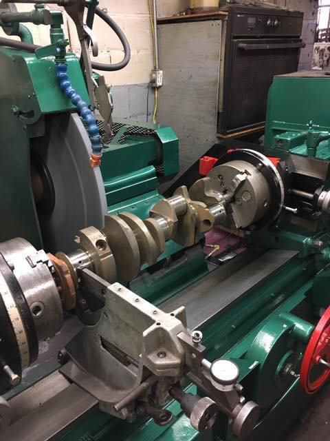 A crankshaft being ground on a green machine in a workshop.