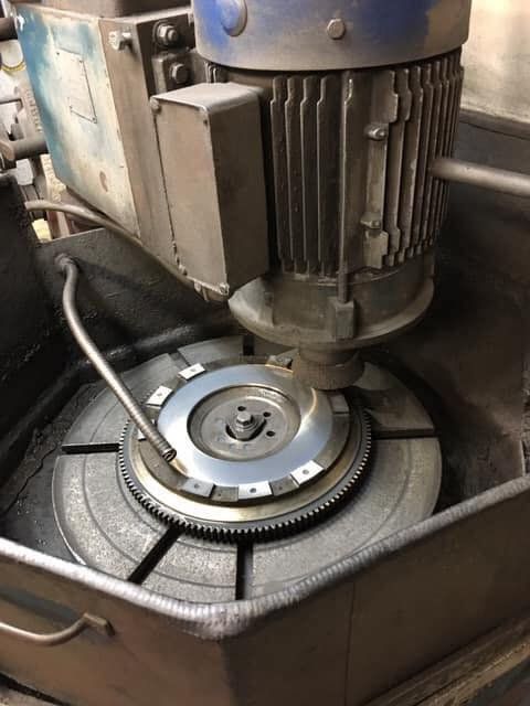 A flywheel being ground on a machine. The device is inside a metal box.