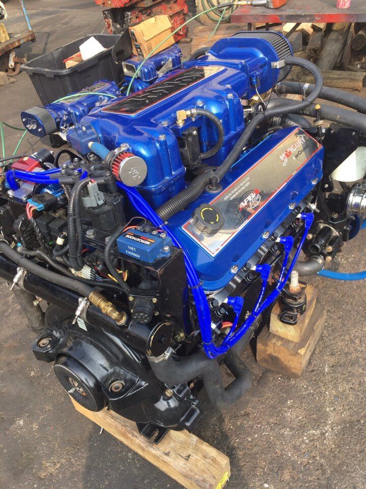 Blue and black marine engine with chrome accents, resting on wooden blocks in a workshop setting.
