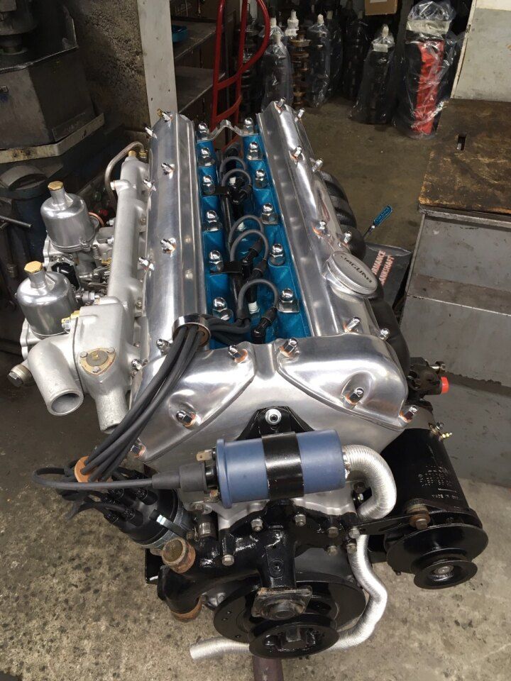 Jaguar engine, blue cylinder head, silver valve covers, black components, workshop setting.