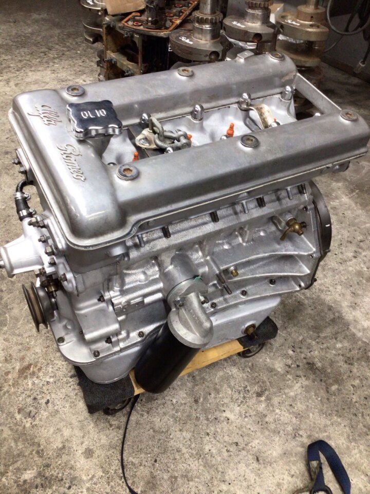 Silver Alfa Romeo engine, viewed from an angle, on a wooden stand in a shop.
