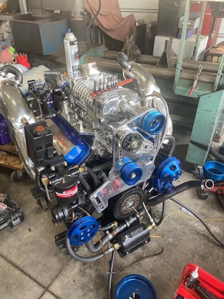 High-performance engine with polished chrome, blue accents, and a supercharger in a workshop setting.