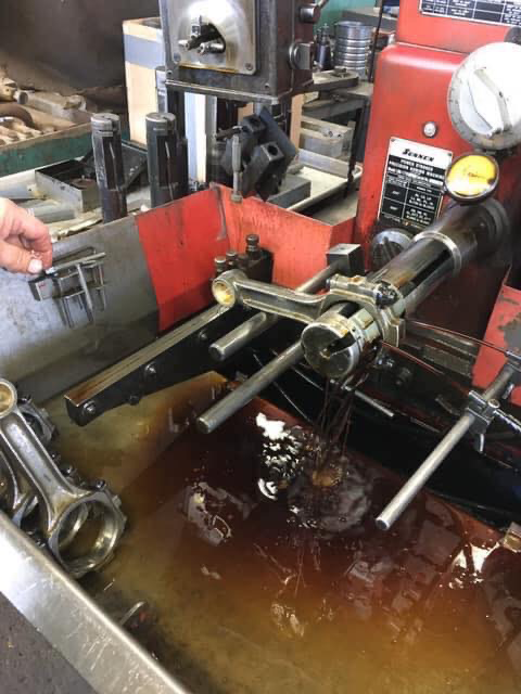 Connecting rods being machined on a red industrial machine, submerged in oil.