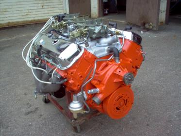 Bright orange V8 engine on a red wheeled stand, with chrome components and two carburetors.