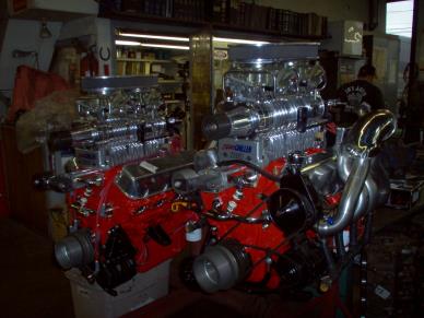 Two red and chrome car engines with large carburetors, in a workshop.