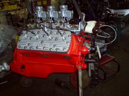 Red Ford flathead engine with triple carburetors in a workshop setting.