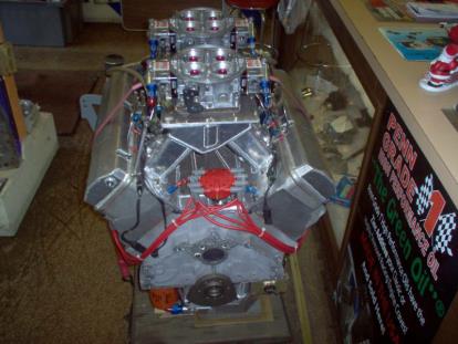 Close-up of a high-performance car engine with multiple carburetors, in a shop setting.
