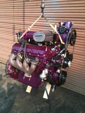 Purple engine hanging, held by straps, in front of a corrugated metal backdrop.