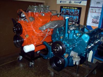 Two car engines, one orange, one teal, on stands indoors.