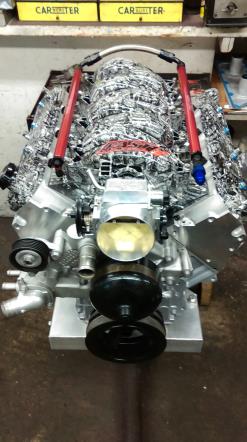 Silver engine with red rods, black pulley, and silver intake manifold in a workshop.