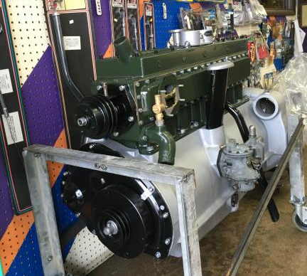Green and silver vintage car engine on a metal stand, displayed in a shop with tools and decor.