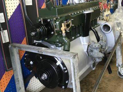 Green and silver vintage car engine on display, with black accessories.