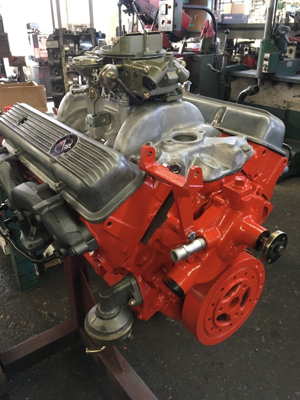 Red and silver engine on a stand in a shop, with carburetor and other components visible.