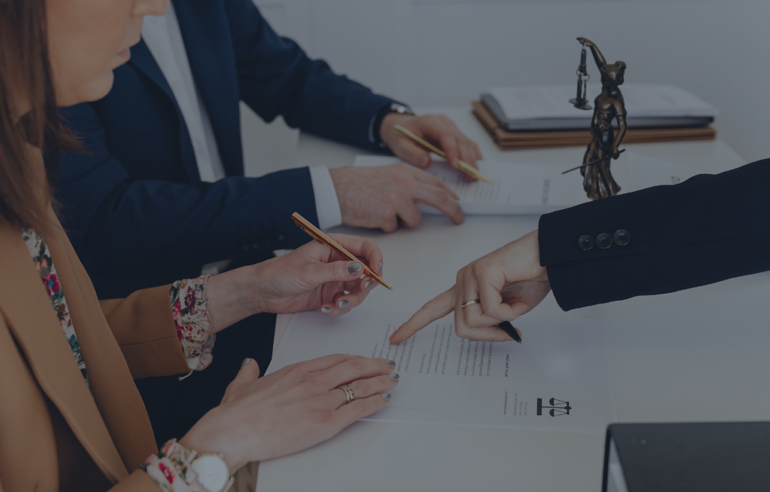 Two people shaking hands over a desk with a laptop and documents near a window.