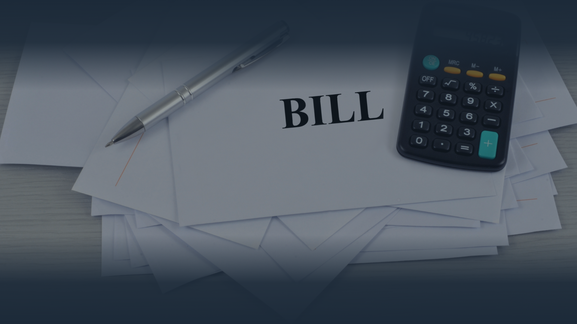 Stack of bills with a pen and calculator on a wooden surface.