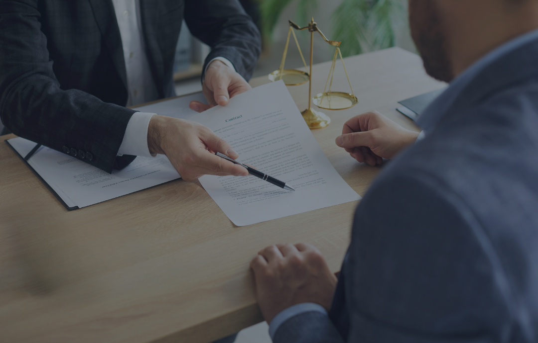 Two people shaking hands over a desk with a laptop and documents near a window.