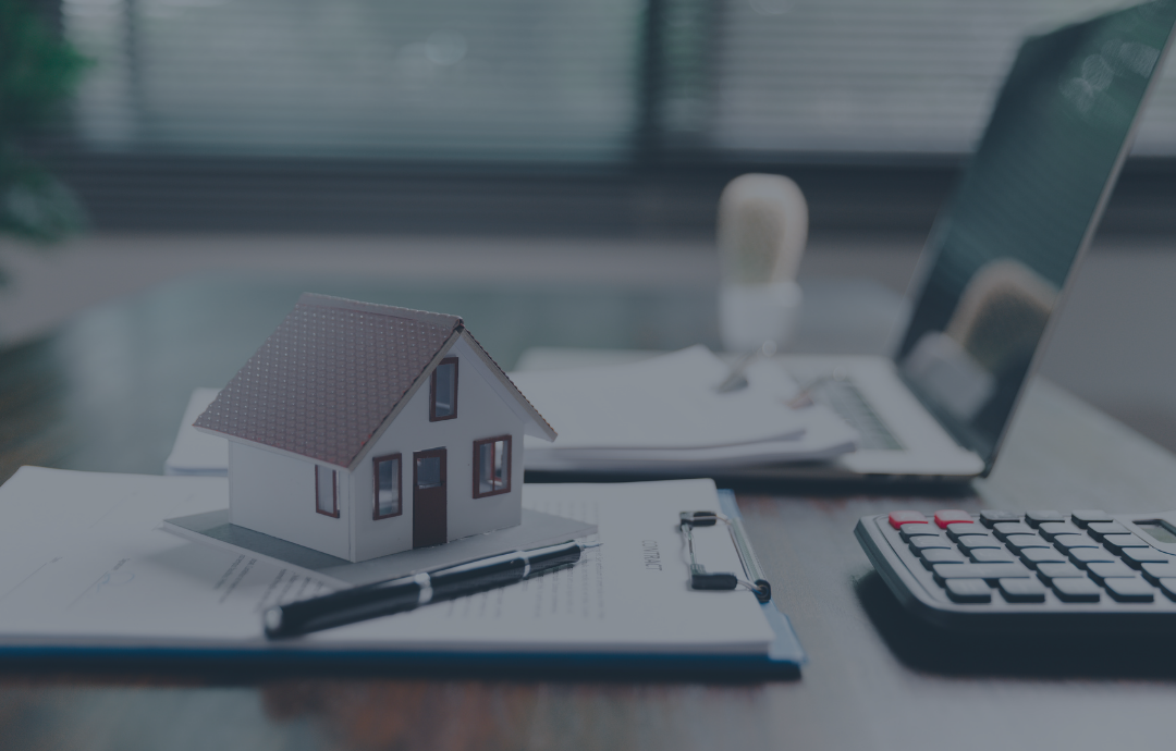 Two people shaking hands over a desk with a laptop and documents near a window.