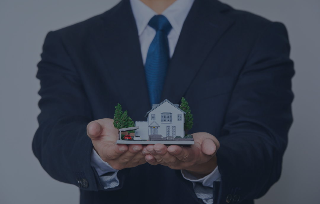 Man in suit holding a miniature house, symbolizing real estate or property ownership.