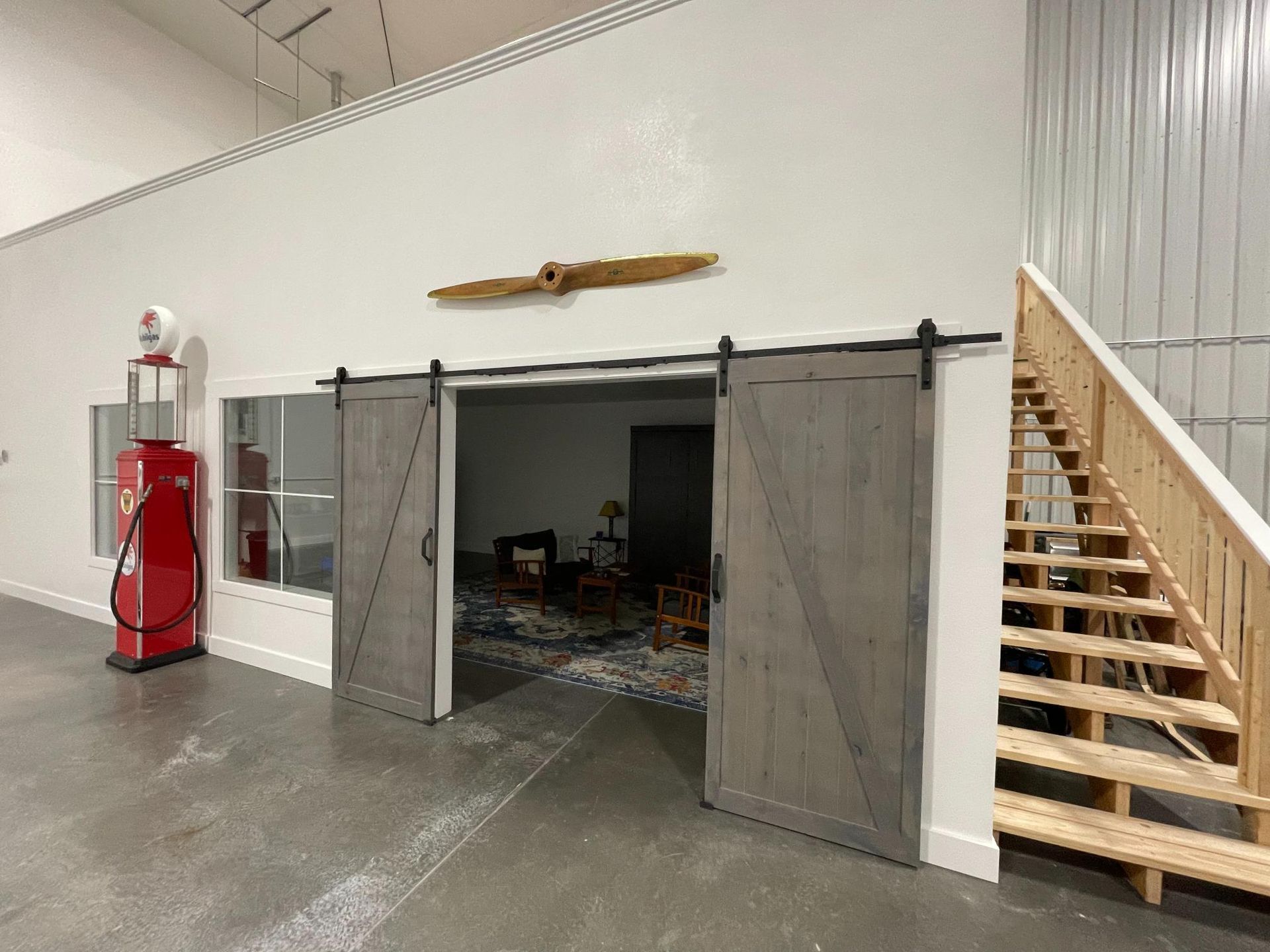Barn doors open into a room, with a propeller above them and a red gas pump on the left. Staircase to the right.