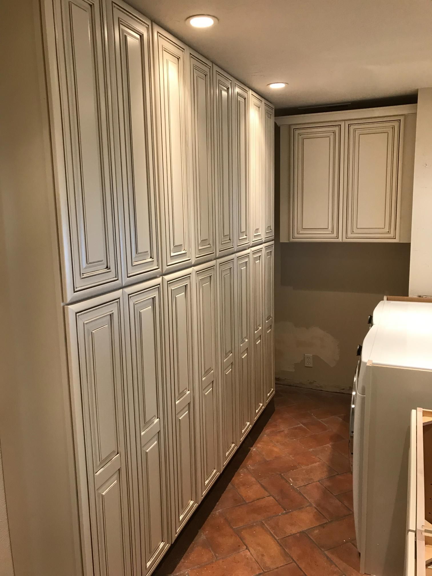 Tall white storage cabinets with patterned doors in a room with terracotta tile flooring.
